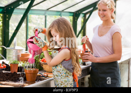 Ragazza giovane nella serra di impianto di irrigazione con la donna holding pot sorridente Foto Stock