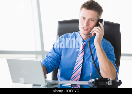 Imprenditore seduto in ufficio con computer laptop utilizzando il telefono Foto Stock