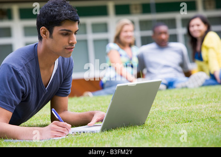 Studente all'aperto sul prato utilizzando laptop con altri studenti di sfondo (il fuoco selettivo) Foto Stock