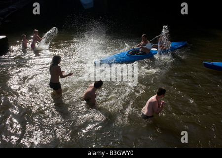 Gettare acqua, bagnanti splash canoisti come essi racchetta in uno stramazzo sulla regione delle Ardenne belghe fiume Lesse, vicino a Dinant. Foto Stock