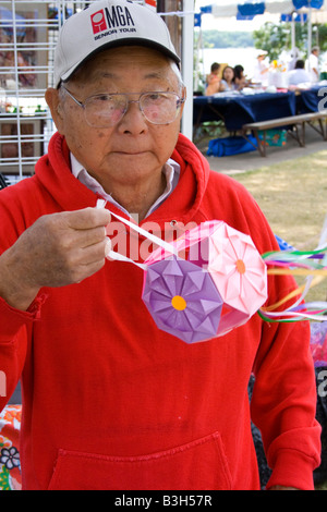 Uomo asiatico holding appeso decorativi lanterna di carta venduti presso il suo stand. Dragon Festival Lago Phalen Park St Paul Minnesota USA Foto Stock