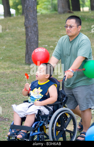 Portatori di handicap fisicamente disabili boy essendo spinto da papà in sedia a rotelle. Dragon Festival Lago Phalen Park St Paul Minnesota USA Foto Stock