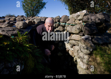 Tatuato eremita Tom Leppard emerge dall'ingresso del suo segreto rifugio improvvisato rifugio a Skye Foto Stock