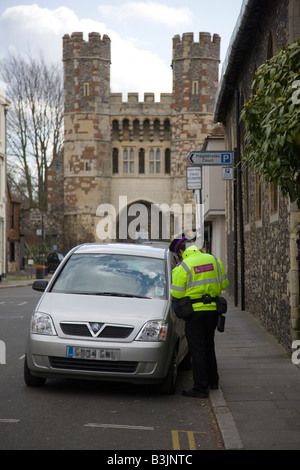 Vigile scrivendo un biglietto destinati ad una macchina parcheggiata sul doppio di linee gialle in una strada in Canterbury Kent Foto Stock