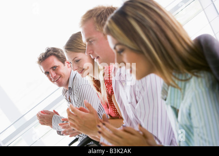 Quattro imprenditori plaudendo all'interno sorridente Foto Stock