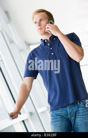 Uomo in piedi nel corridoio sorridente tramite telefono cellulare Foto Stock