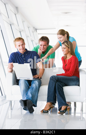 Quattro persone nel lobby e puntando al computer che sorride Foto Stock