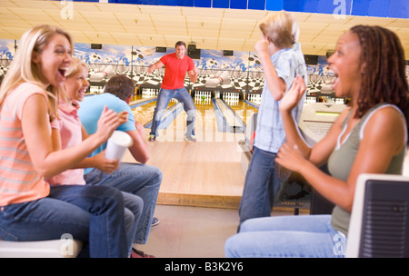 Famiglia in pista da bowling con due amici a fare il tifo e sorridente Foto Stock