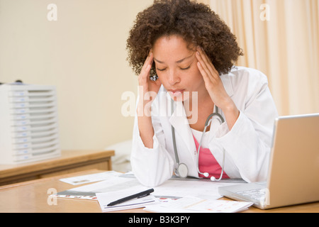 Medico con laptop e mal di testa nell'ufficio del medico Foto Stock