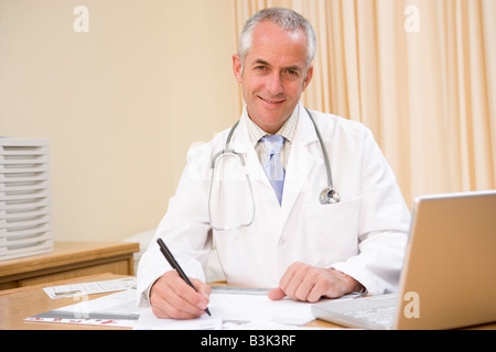 Medico con laptop iscritto nell'ufficio del medico Foto Stock