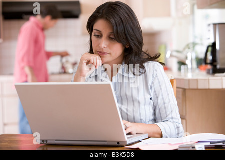 La donna in cucina con pratiche utilizzando laptop con uomo sullo sfondo Foto Stock