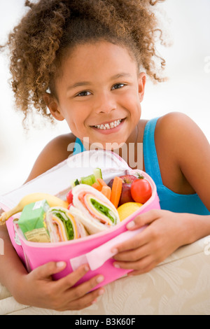 Ragazza giovane azienda il pranzo al sacco nel soggiorno sorridente Foto Stock