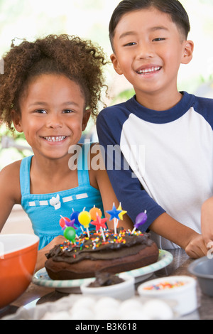 Due bambini in cucina con torta di compleanno sorridente Foto Stock
