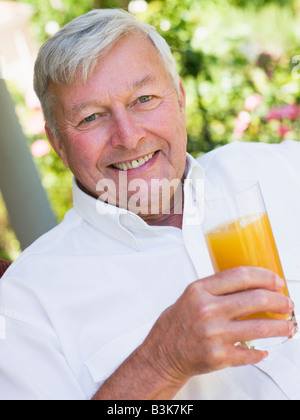 Senior uomo seduto all'aperto con un bicchiere di succo di arancia Foto Stock