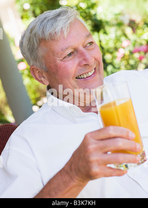 Senior uomo seduto all'aperto con un bicchiere di succo di arancia Foto Stock