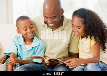 Uomo e due bambini seduti nella sala lettura prenota e sorridente Foto Stock