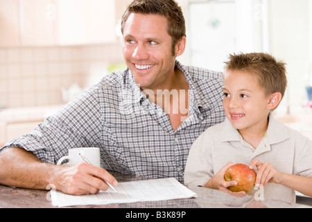 L uomo e il giovane ragazzo in cucina con apple di giornale e caffè sorridente Foto Stock