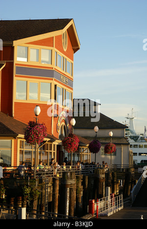 Seattle Waterfront Restaurant su palificate con cestelli appesi visualizzati con il sole di setting e traghetto attraccato in background Foto Stock