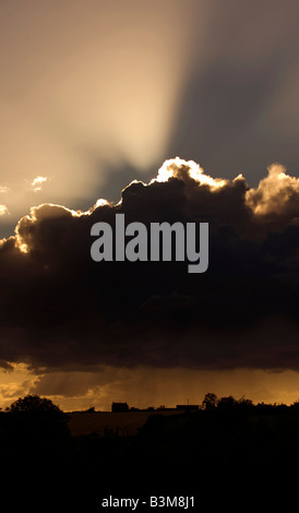 I raggi luminosi di una impostazione di burst di sole fuori da una tempesta di cloud che incessantemente cascades la pioggia sulla terra agricola al di sotto di Foto Stock