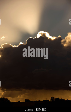 I raggi luminosi di una impostazione di burst di sole fuori da una tempesta di cloud che incessantemente cascades la pioggia sulla terra agricola al di sotto di Foto Stock