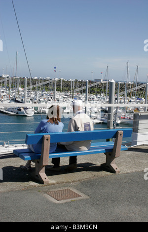 Nautica scena con un uomo anziano e la giovane donna seduta insieme sul sedile unico affacciato sul porto con barche e yacht ormeggiati Foto Stock