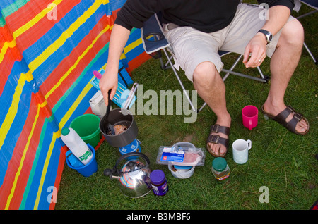 Uomo di pancetta di cottura in un tegame su un fornello da campeggio all'esterno,insieme ad altri bit di campeggio e bobs Foto Stock