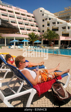 Un giovane giacciono su sedie a sdraio di fronte un hotel piscina, Portogallo. Foto Stock