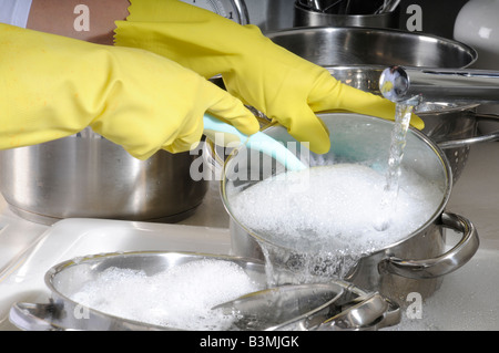 Il lavaggio di pentole e tegami indossando guanti di gomma Foto Stock