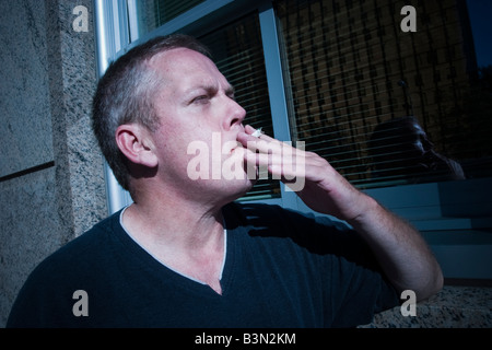 La mezza età uomo fumare una sigaretta poste di fronte ad un edificio Modello rilasciato Foto Stock