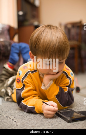 Little Boy gioca il gioco di logica su un pocket PC (PPC) sulla home contesto Foto Stock