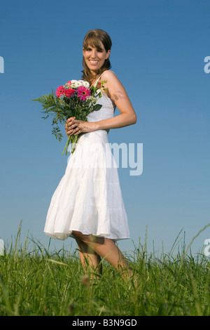 In Germania, in Baviera, giovane donna sul prato, tenendo mazzo di fiori, sorridente, ritratto Foto Stock
