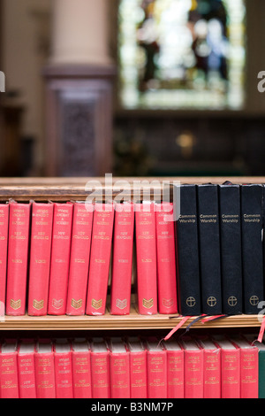 Red inno libri e bibbie impilati su un ripiano contro banchi in una chiesa Foto Stock