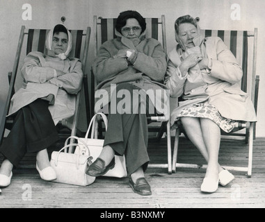 Tre donne i turisti sono tutti avvolti in cappotti e sciarpe come essi combattere fuori il vento e la pioggia donne seduti su sedie a sdraio sfidando il freddo meteo inglese Luglio 1977 Caption locale friendshipimages Foto Stock