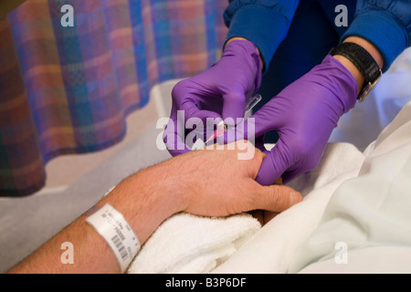 L'infermiera inserendo un tubo IV in un maschio di mano del paziente Foto Stock