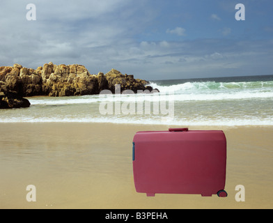 Studio tagliato fuori ancora in vita una valigia rossa in piedi su una spiaggia deserta Foto Stock