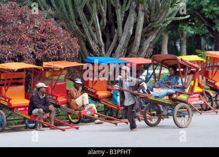 Madagascar, Southern Highlands, dipinto luminosamente rickshaws o pousse-pousse su un ampio viale in Antsirabe. Antsirabe è il ind Foto Stock
