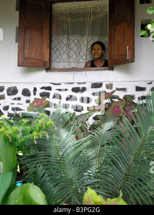 Madagascar settentrionale, un malgascio donna guarda fuori dalla finestra della sua attraente casa a Ramena, un villaggio di pescatori che si trova a breve distanza da Antsiranana, più comunemente noto come Diego.Ha il viso coperto con un impasto costituito da polvere di legno e semi di un albero speciale per evitare scottature. Questa forma di protezione dal sole è molto comune tra le donne che lavorano nelle risaie tutto il giorno. Foto Stock