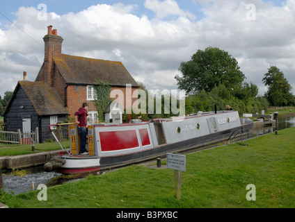 Uomo sulla poppa della tradizionale narrowboat passando attraverso il blocco Triggs sul fiume Wey Navigazione, vicino a Woking, Surrey, Inghilterra Foto Stock