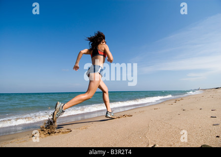 Modello rilasciato montare giovane donna in corsa lungo la riva di un vuoto spiaggia sabbiosa Foto Stock