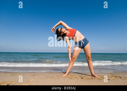 Modello rilasciato montare giovane donna facendo esercizi di stretching su di una spiaggia di sabbia Foto Stock