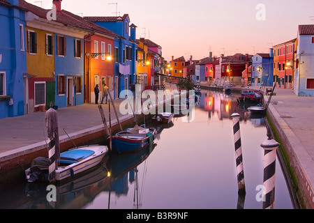 Burano Venezia Italia canal riflessioni al tramonto con barche e colorate case di pescatori riflettendo su acqua a cielo chiaro Foto Stock