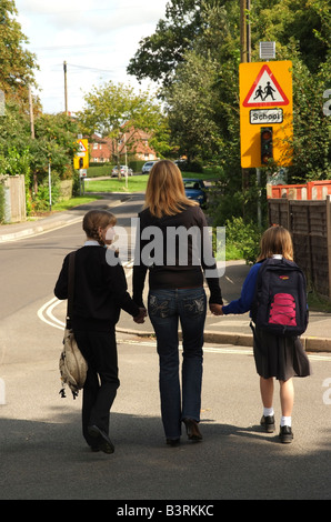 Madre e bambini andare a scuola a piedi lungo un marciapiede Foto Stock