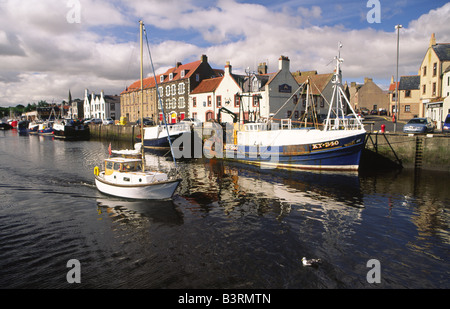 Piccolo yacht lasciando un pittoresco Eyemouth Harbour barche da pesca e la città dietro con Berwickshire Scottish Borders Scotland Regno Unito Foto Stock