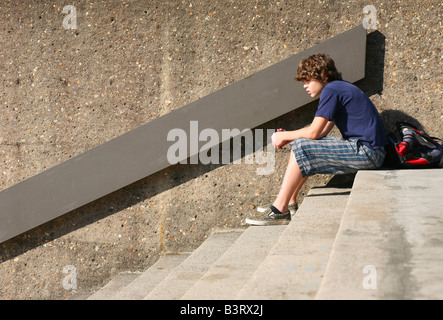 Un pre-adolescenti giovane ragazzo si trova in cima a scale di cemento, curvò su profondamente pensando...l'adolescenza--un tempo di grande cambiamento! Foto Stock