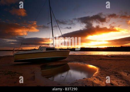 Barca in appoggio su un sandbank a bassa marea in Alnmouth estruary l'ansa tramonto si riflette in una piscina di acqua Foto Stock