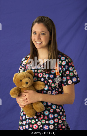 Giovane donna in pazienti pediatrici nurse scrubs con un orsacchiotto e stetoscopio Foto Stock