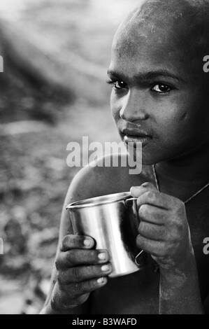 Povero ragazzo indiano con tazza di metallo, acqua potabile. In bianco e nero Foto Stock
