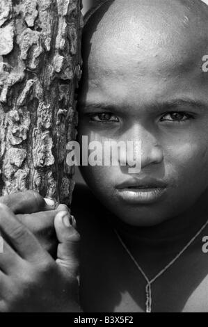 Povero ragazzo indiano appoggiato contro l'albero, in bianco e nero. Foto Stock