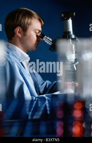 Il tecnico di controllo campioni di acqua attraverso un microscopio nel laboratorio di controllo qualità di un impianto di trattamento dell'acqua. Foto Stock