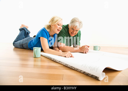 Coppia di mezza età che giace sul piano esaminando e discutendo gli schemi architetturali insieme Foto Stock